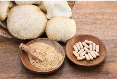 Cogumelo Juba de Leão in natura, em pó e em cápsulas, distribuídos em vasilhas sobre uma mesa de madeira. 