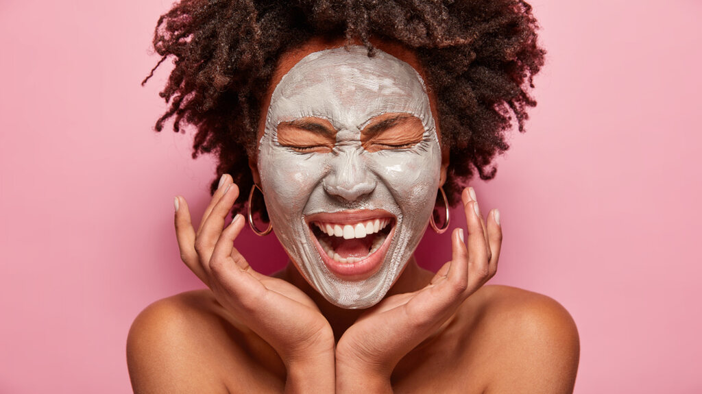 Como preparar argila preta, mulher sorridente realizando tratamento cosmético com argila preta