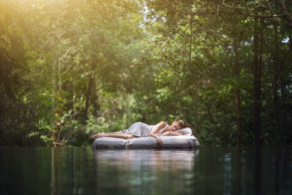 Mulher boiando em um colchão inflável em um lago em meio a floresta